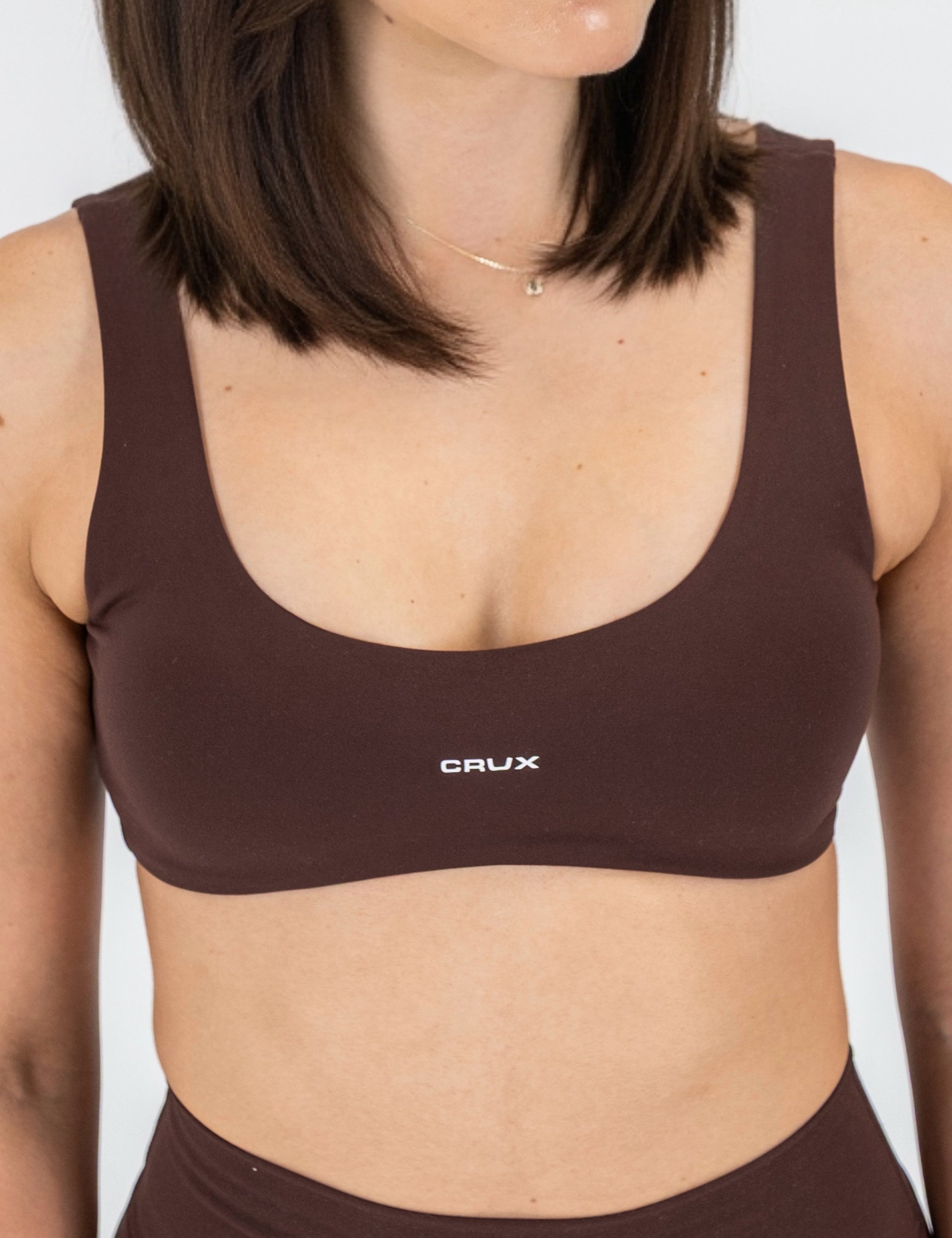 Woman wearing a brown sports bra with 'CRUX' branding on a white background