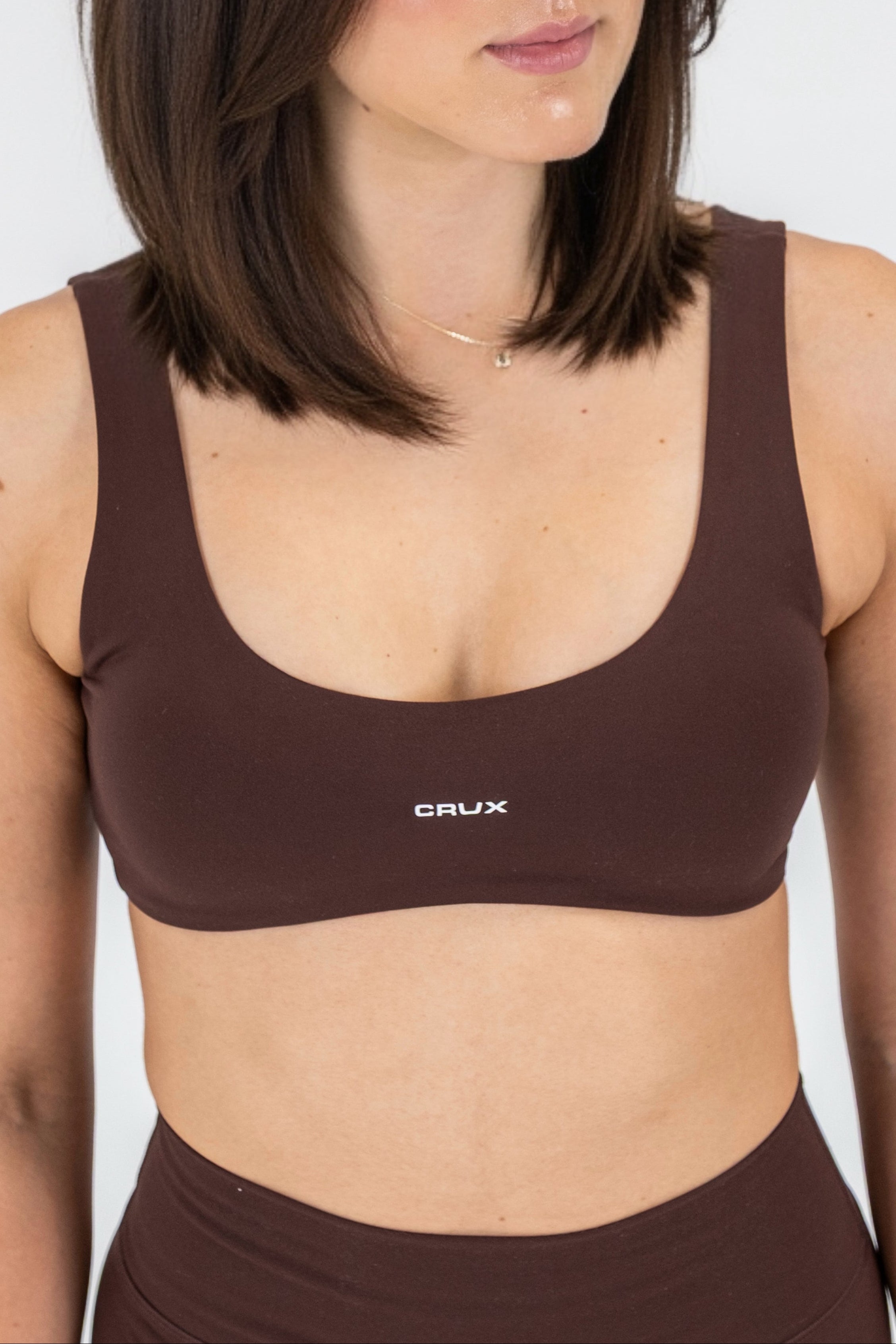 Woman wearing a brown sports bra with 'CRUX' branding on a white background
